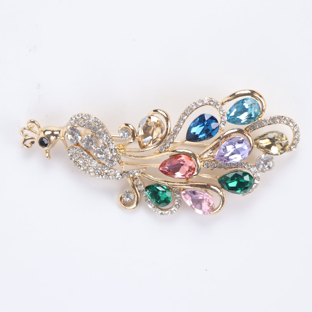 Sparkling gold peacock brooch pin adorned with colorful teardrop-cut crystals and clear pavé rhinestones against a white background by Delemon