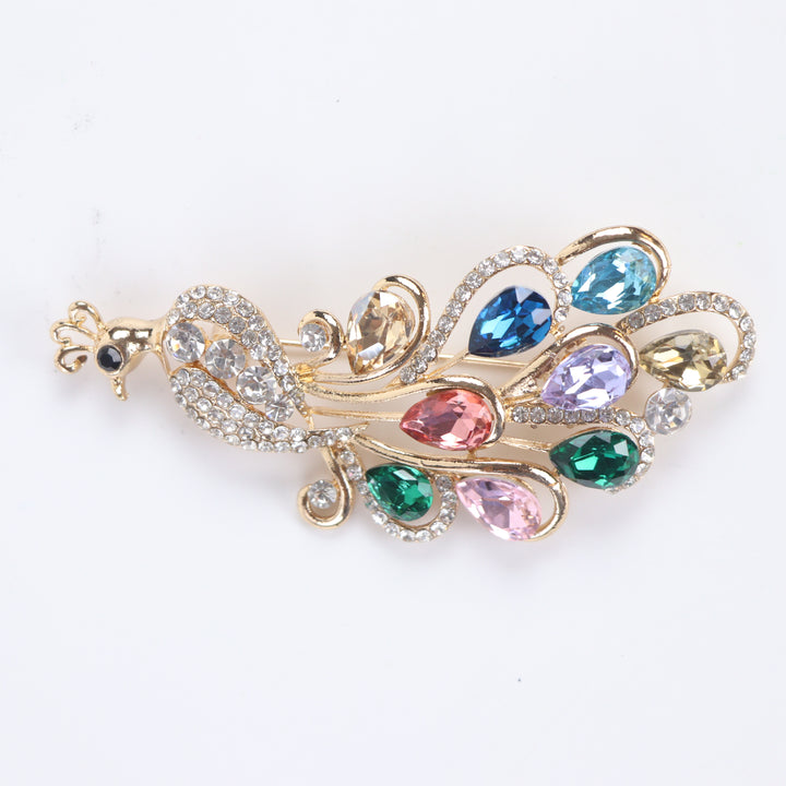 Sparkling gold peacock brooch pin adorned with colorful teardrop-cut crystals and clear pavé rhinestones against a white background by Delemon
