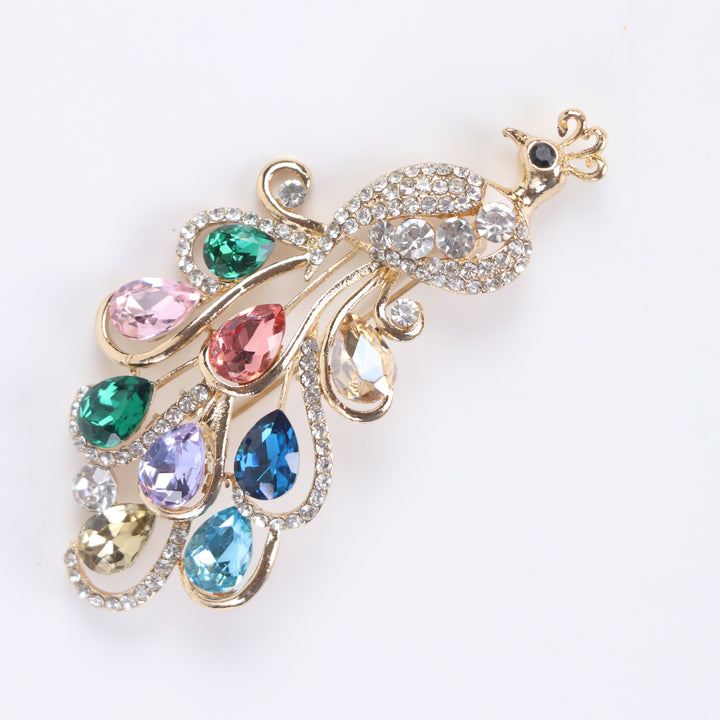 Sparkling gold peacock brooch pin adorned with colorful teardrop-cut crystals and clear pavé rhinestones against a white background by Delemon