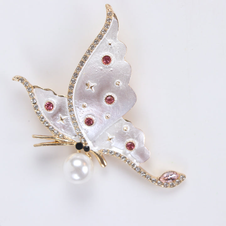 Pearlescent white enamel butterfly brooch pin with a large pearl accent and pink crystals against a white background by Delemon