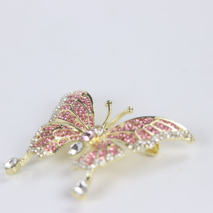 Sparkling gold butterfly brooch pin embellished with pink and clear crystals on a white background by Delemon