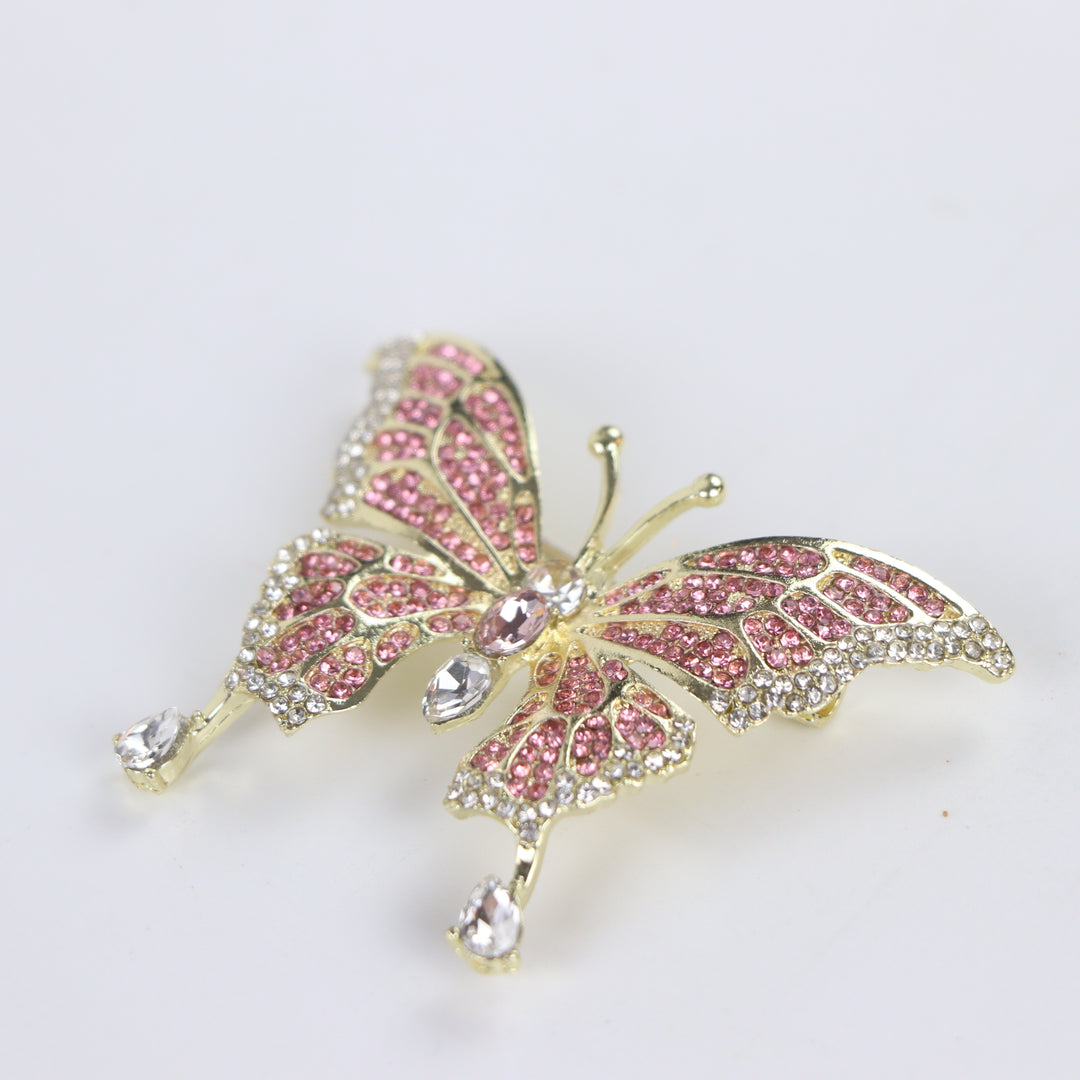 Sparkling gold butterfly brooch pin embellished with pink and clear crystals on a white background by Delemon