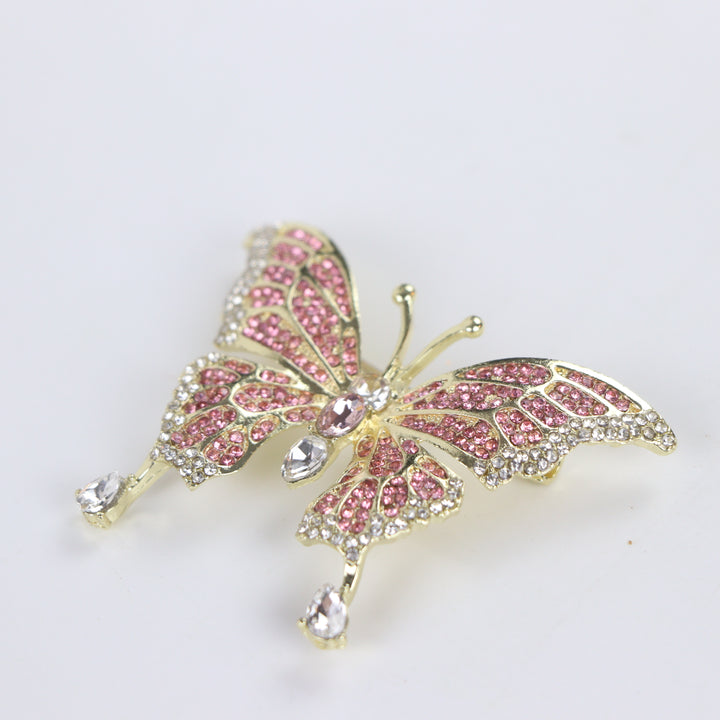 Sparkling gold butterfly brooch pin embellished with pink and clear crystals on a white background by Delemon