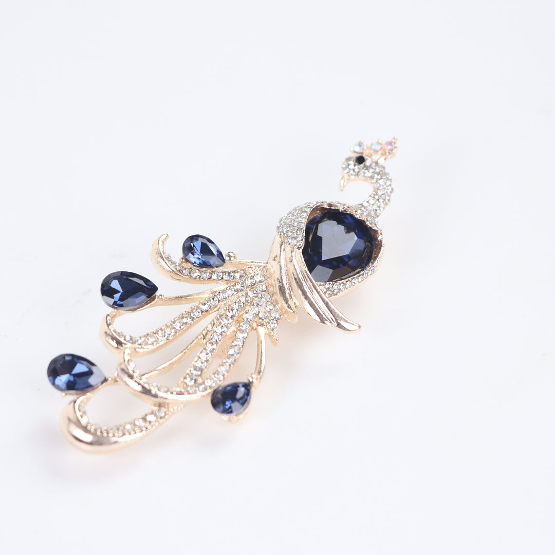 Majestic peacock brooch pin with clear pavé crystals and deep blue teardrop gems on a white background by Delemon