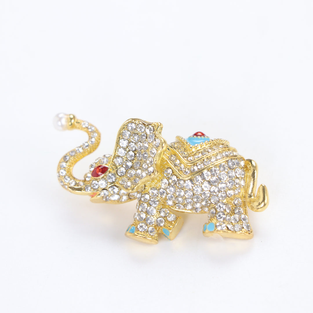 Sparkling gold elephant brooch pin with paved crystals, turquoise enamel saddle, and a pearl trunk tip on a white background by Delemon