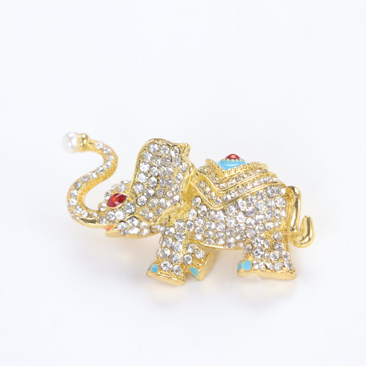Sparkling gold elephant brooch pin with paved crystals, turquoise enamel saddle, and a pearl trunk tip on a white background by Delemon