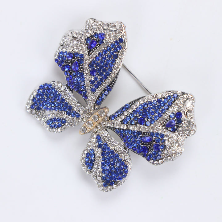 Sparkling silver-tone butterfly brooch pin encrusted with sapphire blue and clear crystals on a white background by Delemon