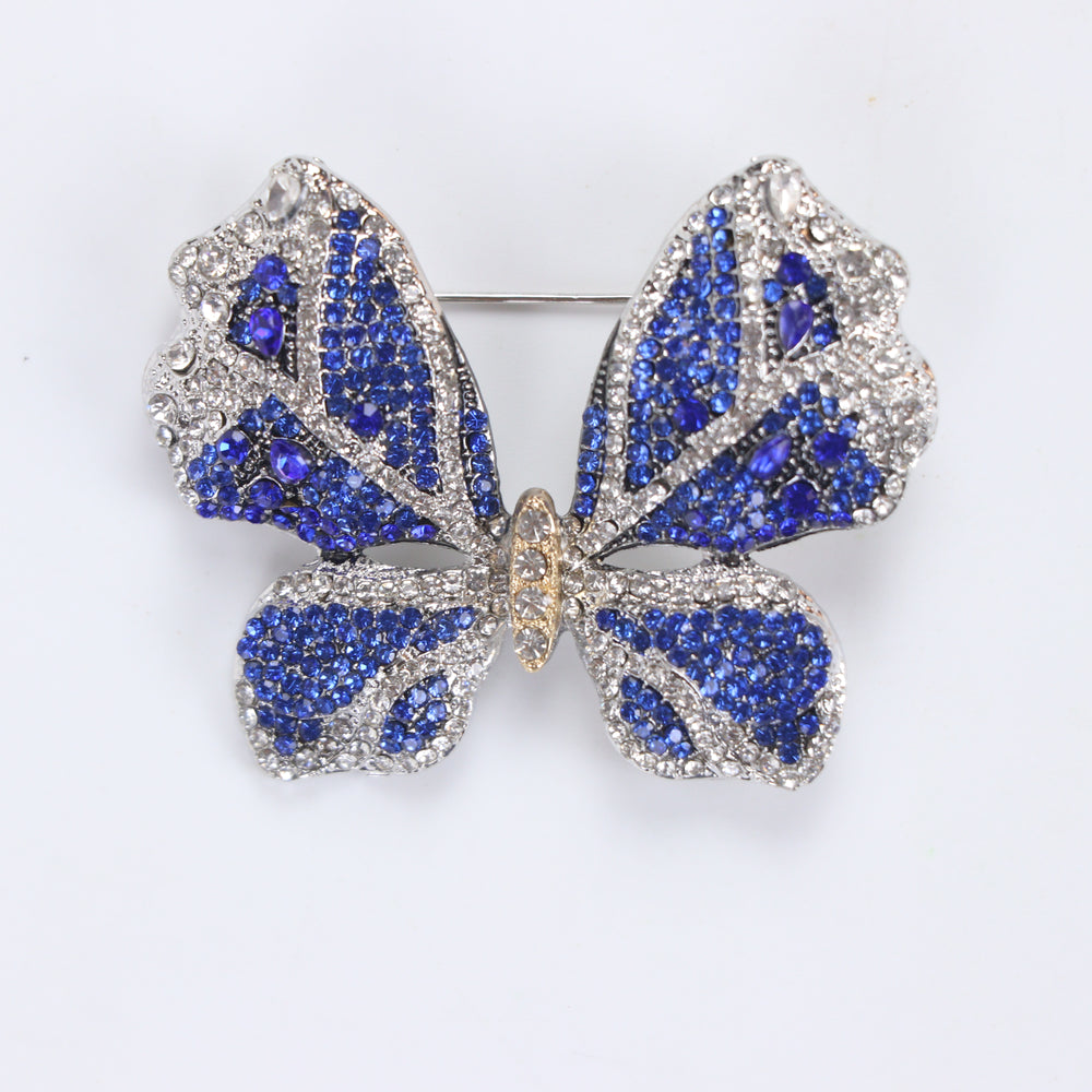 Sparkling silver-tone butterfly brooch pin encrusted with sapphire blue and clear crystals on a white background by Delemon