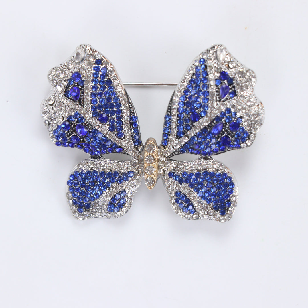 Sparkling silver-tone butterfly brooch pin encrusted with sapphire blue and clear crystals on a white background by Delemon
