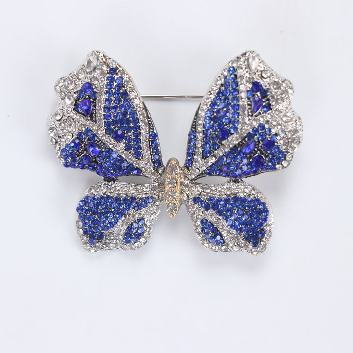 Sparkling silver-tone butterfly brooch pin encrusted with sapphire blue and clear crystals on a white background by Delemon