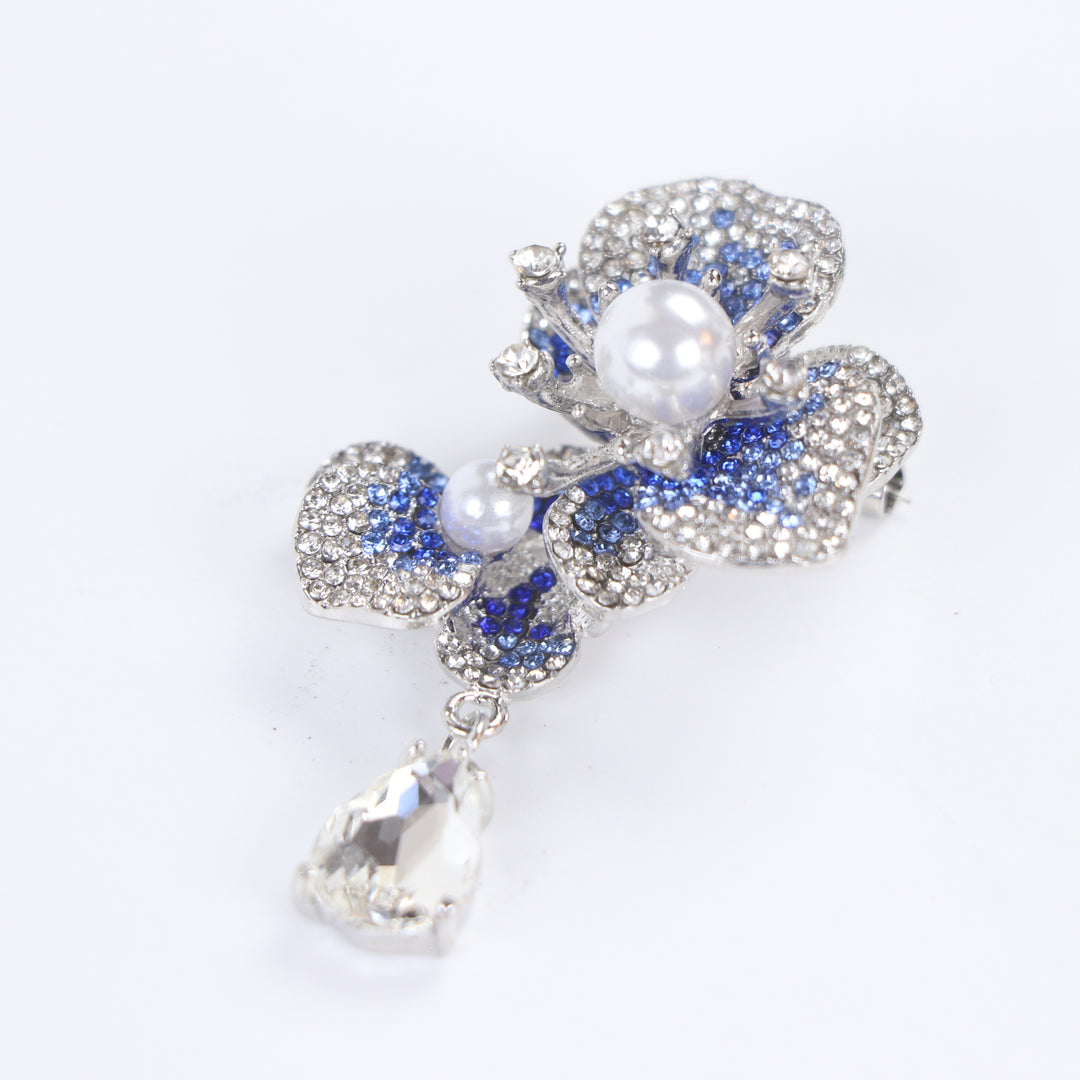 Silver-tone sapphire blue crystal orchid flower brooch pin with pearl centers and a dangling teardrop crystal on a white background by Delemon