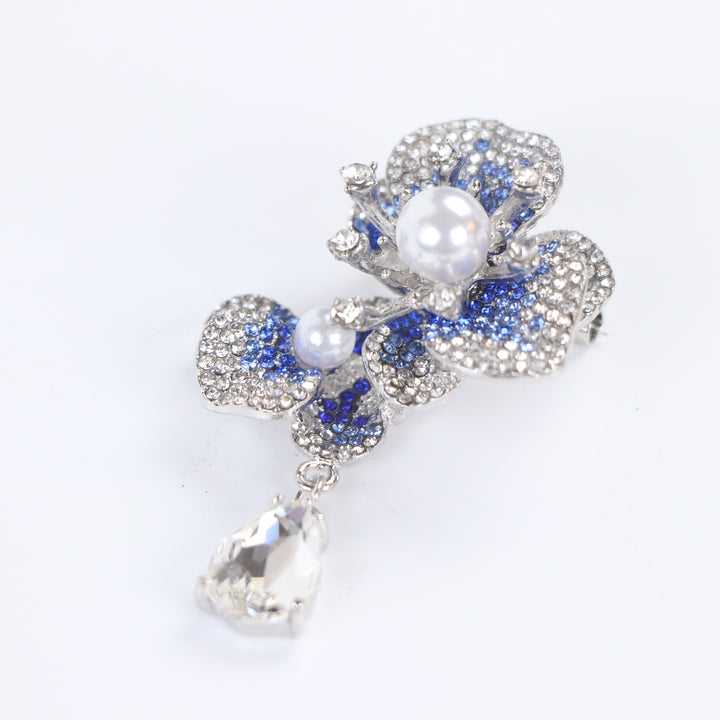 Silver-tone sapphire blue crystal orchid flower brooch pin with pearl centers and a dangling teardrop crystal on a white background by Delemon