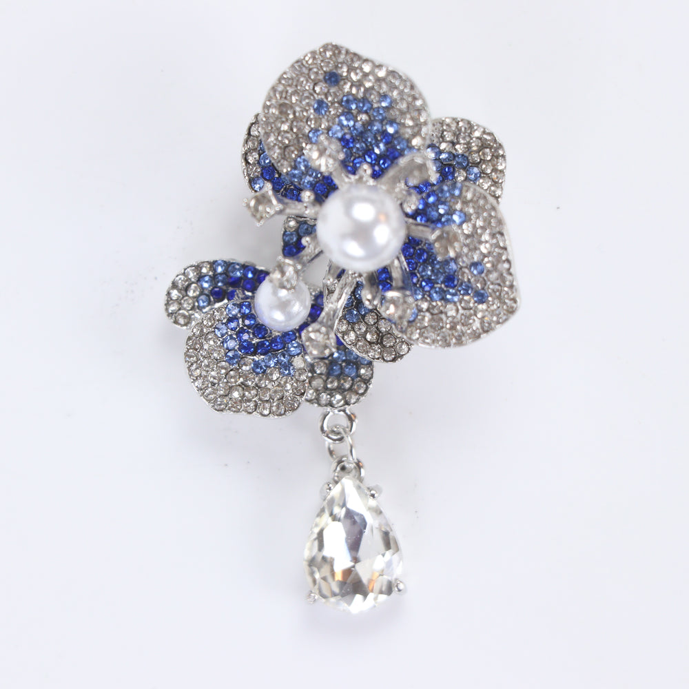 Silver-tone sapphire blue crystal orchid flower brooch pin with pearl centers and a dangling teardrop crystal on a white background by Delemon