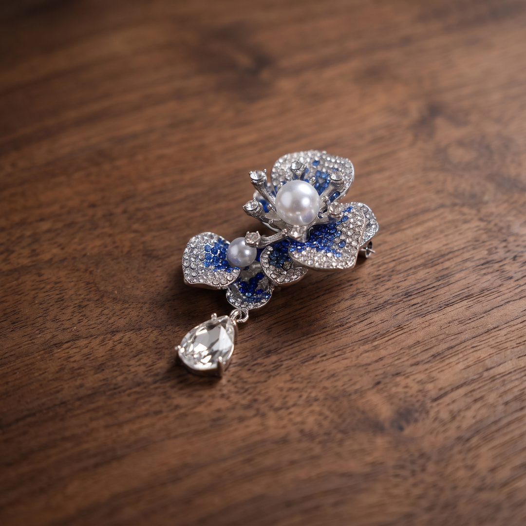 Silver-tone sapphire blue crystal orchid flower brooch pin with pearl centers and a dangling teardrop crystal 