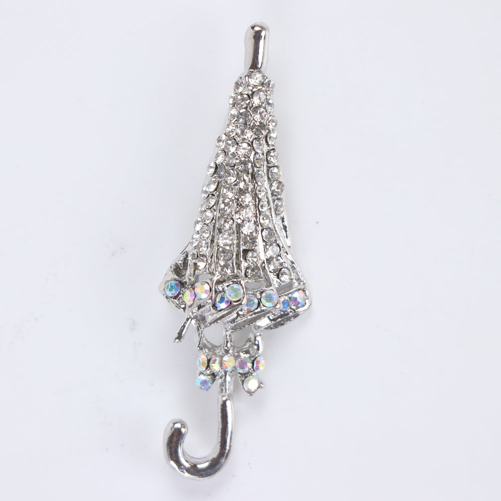 Silver-tone folded umbrella brooch pin encrusted with clear pavé crystals and iridescent rhinestone trim on a white background by Delemon