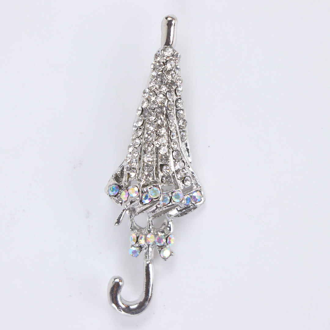 Silver-tone folded umbrella brooch pin encrusted with clear pavé crystals and iridescent rhinestone trim on a white background by Delemon