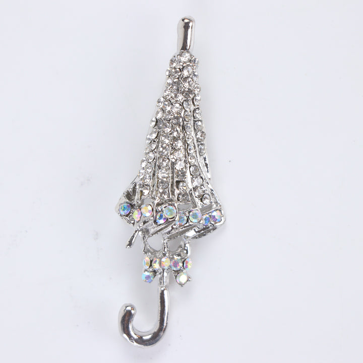 Silver-tone folded umbrella brooch pin encrusted with clear pavé crystals and iridescent rhinestone trim on a white background by Delemon