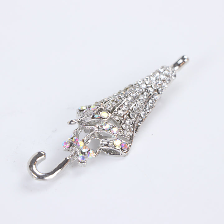 Silver-tone folded umbrella brooch pin encrusted with clear pavé crystals and iridescent rhinestone trim on a white background by Delemon
