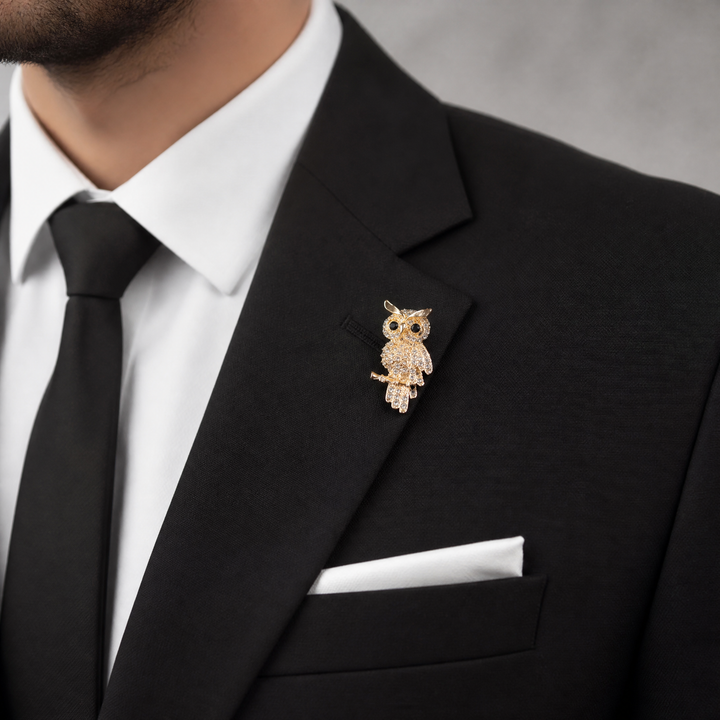 Gold owl brooch pin encrusted with clear crystals and black crystal eyes perched on a branch against a white background by Delemon