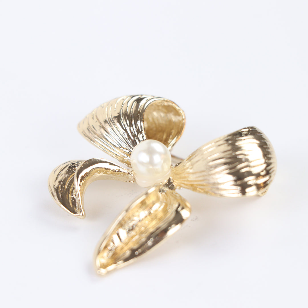 Textured gold ribbon bow brooch pin featuring a centered pearl accent against a white background by Delemon