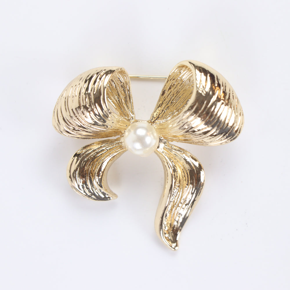 Textured gold ribbon bow brooch pin featuring a centered pearl accent against a white background by Delemon