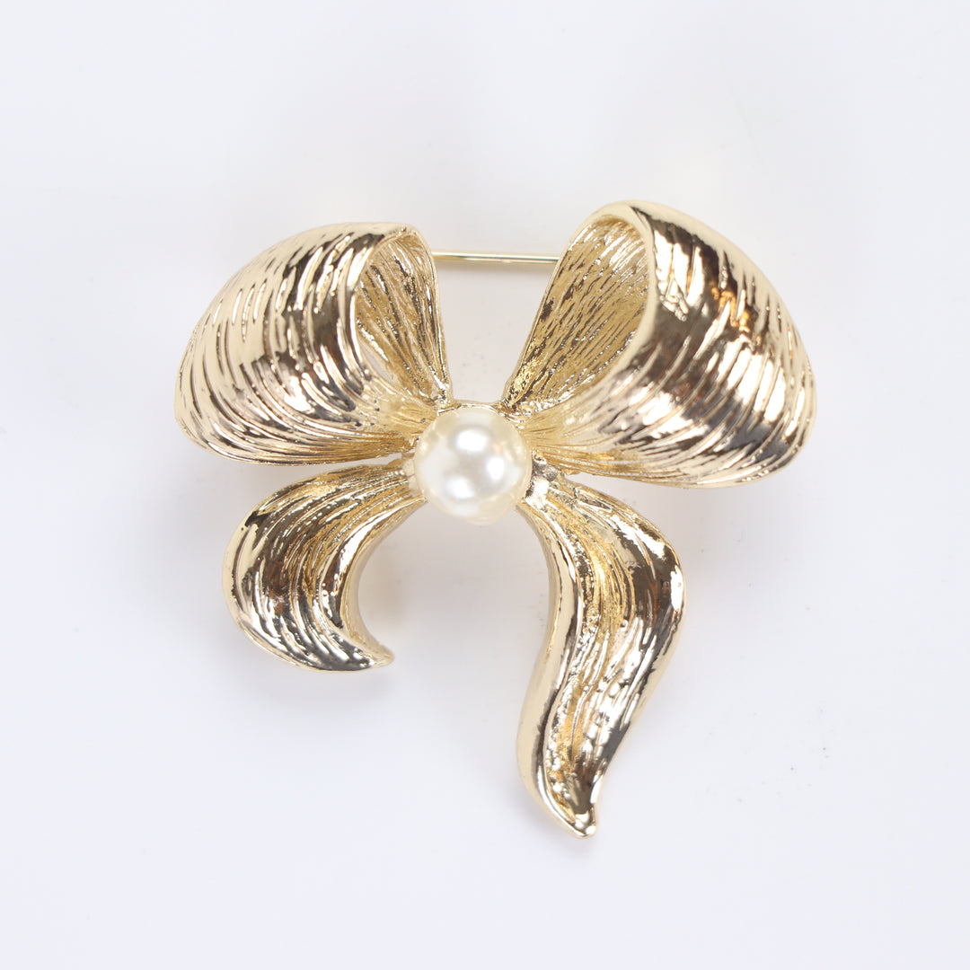 Textured gold ribbon bow brooch pin featuring a centered pearl accent against a white background by Delemon