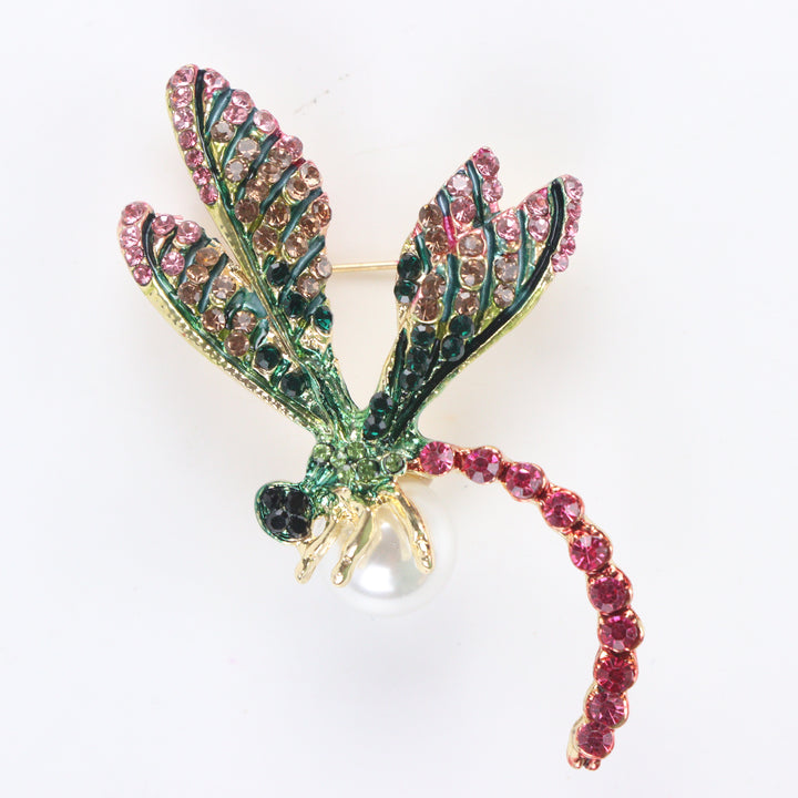 Gold-tone dragonfly brooch pin with pink and green rhinestone wings, fuchsia crystal tail, and a white pearl on a white background by Delemon