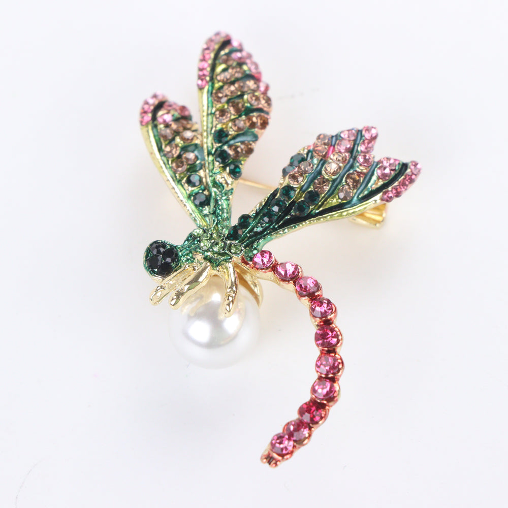Gold-tone dragonfly brooch pin with pink and green rhinestone wings, fuchsia crystal tail, and a white pearl on a white background by Delemon