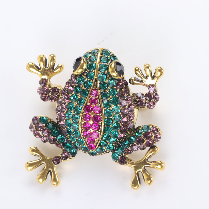 Antique gold-tone tree frog brooch pin encrusted with emerald green, purple, and hot pink crystals on a white background by Delemon