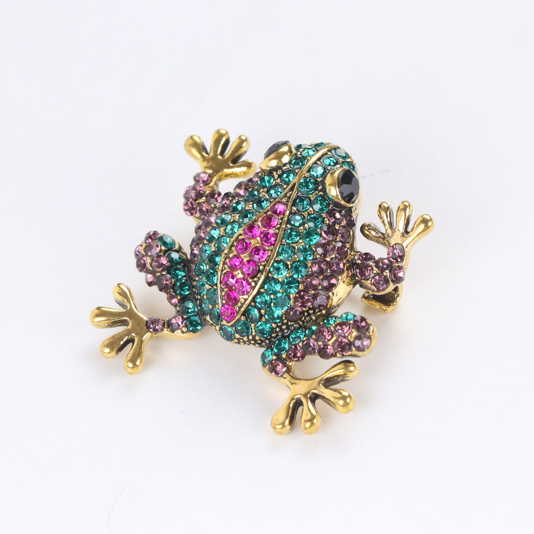 Antique gold-tone tree frog brooch pin encrusted with emerald green, purple, and hot pink crystals on a white background by Delemon