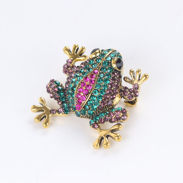 Antique gold-tone tree frog brooch pin encrusted with emerald green, purple, and hot pink crystals on a white background by Delemon