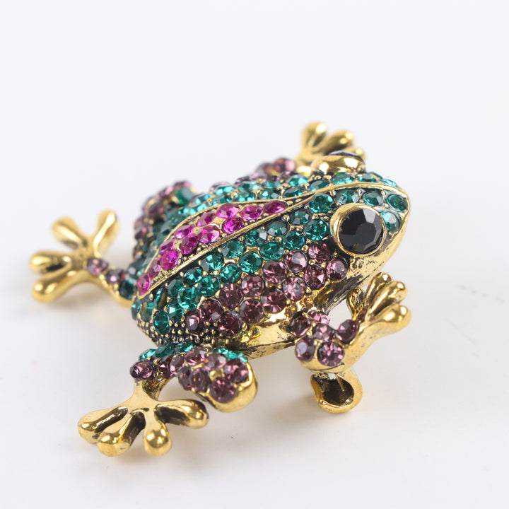 Antique gold-tone tree frog brooch pin encrusted with emerald green, purple, and hot pink crystals on a white background by Delemon