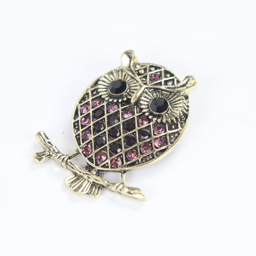 Vintage antique gold owl brooch pin with purple crystal lattice body and black crystal eyes on a branch against a white background by Delemon