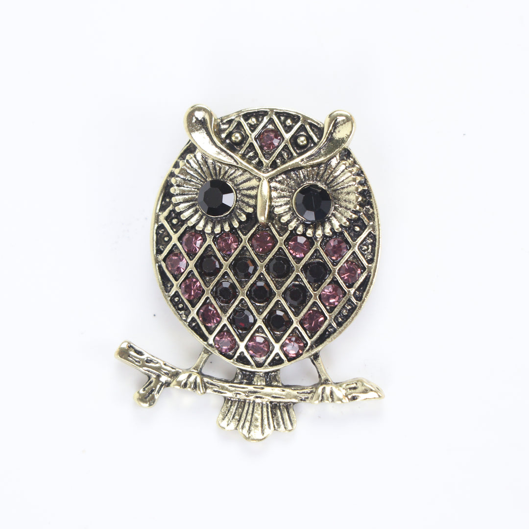 Vintage antique gold owl brooch pin with purple crystal lattice body and black crystal eyes on a branch against a white background by Delemon