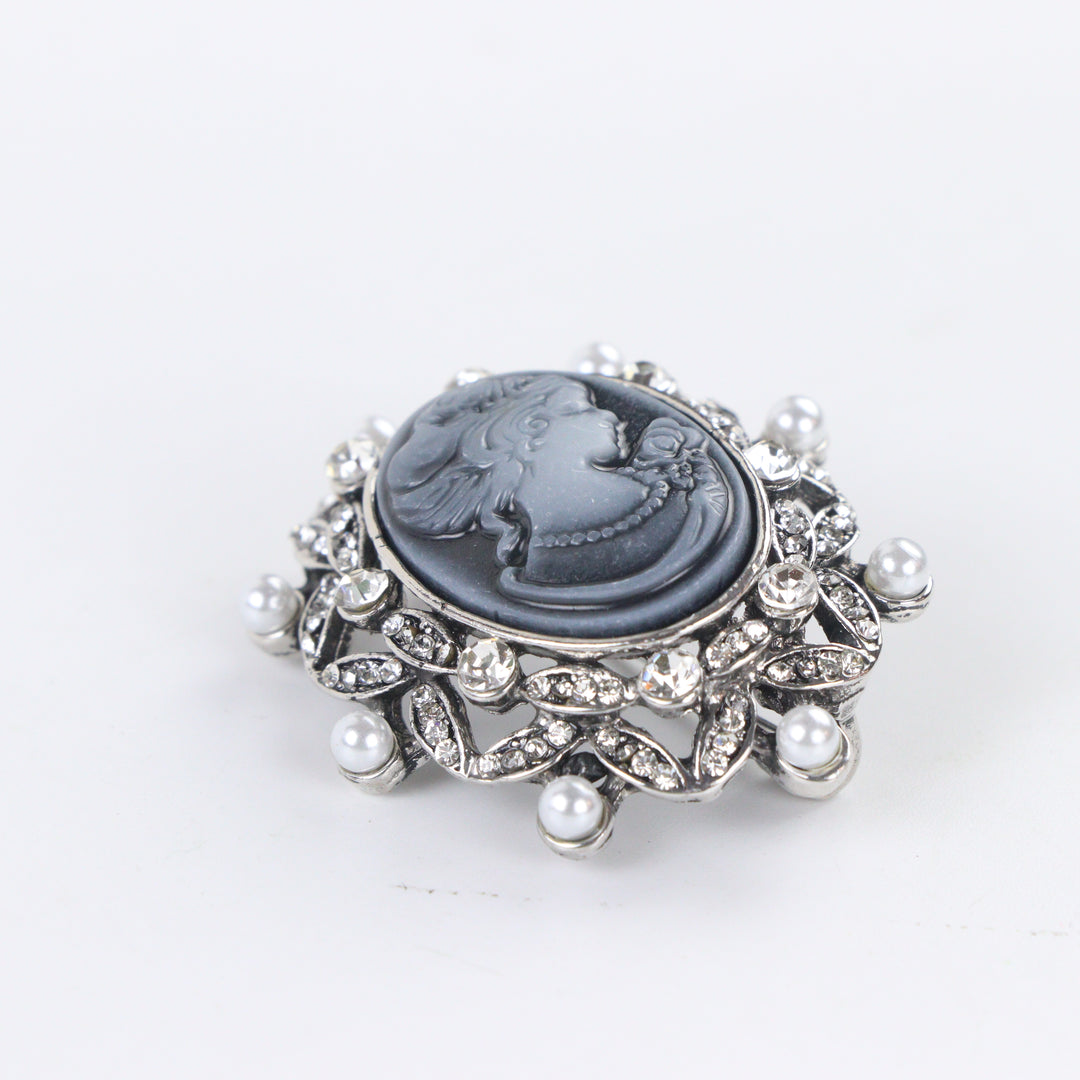 Antique silver-tone oval cameo brooch pin featuring a carved lady profile, clear rhinestones, and pearl trim on a white background by Delemon