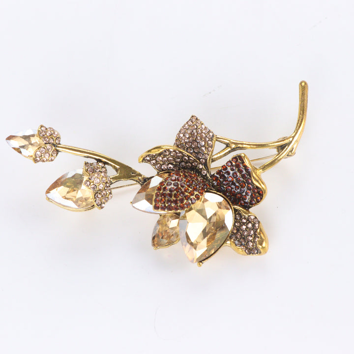 Antiqued gold-tone floral branch brooch pin featuring champagne crystals, topaz rhinestones, and crystal buds on a white background by Delemon