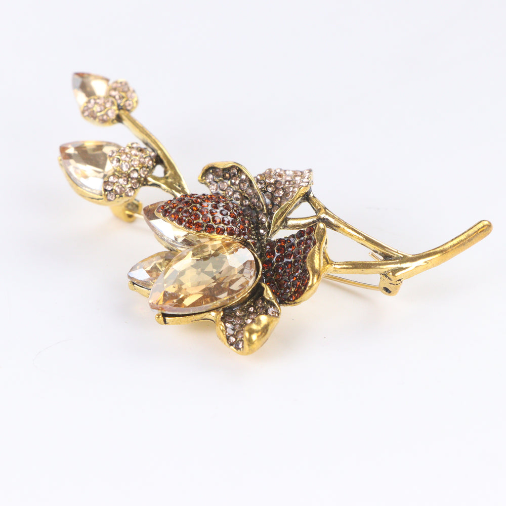 Antiqued gold-tone floral branch brooch pin featuring champagne crystals, topaz rhinestones, and crystal buds on a white background by Delemon
