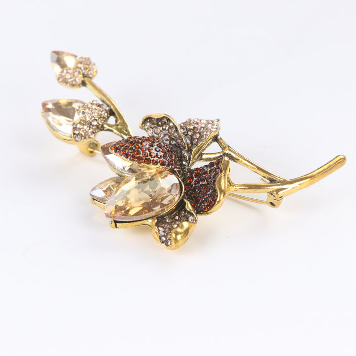 Antiqued gold-tone floral branch brooch pin featuring champagne crystals, topaz rhinestones, and crystal buds on a white background by Delemon