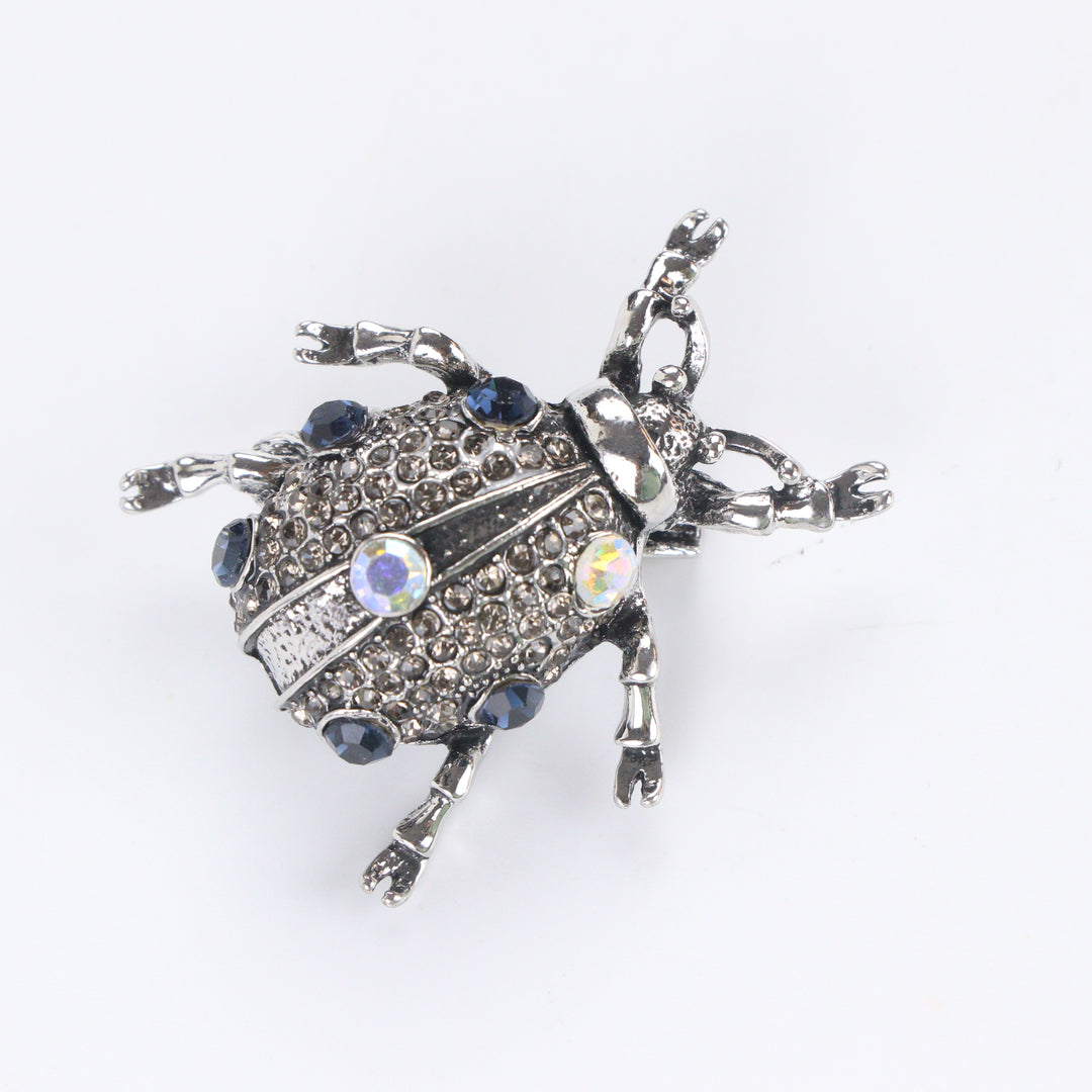 Antiqued silver-tone beetle brooch pin pavé-set with smoky rhinestones, blue crystals, and iridescent gems on a white background by Delemon