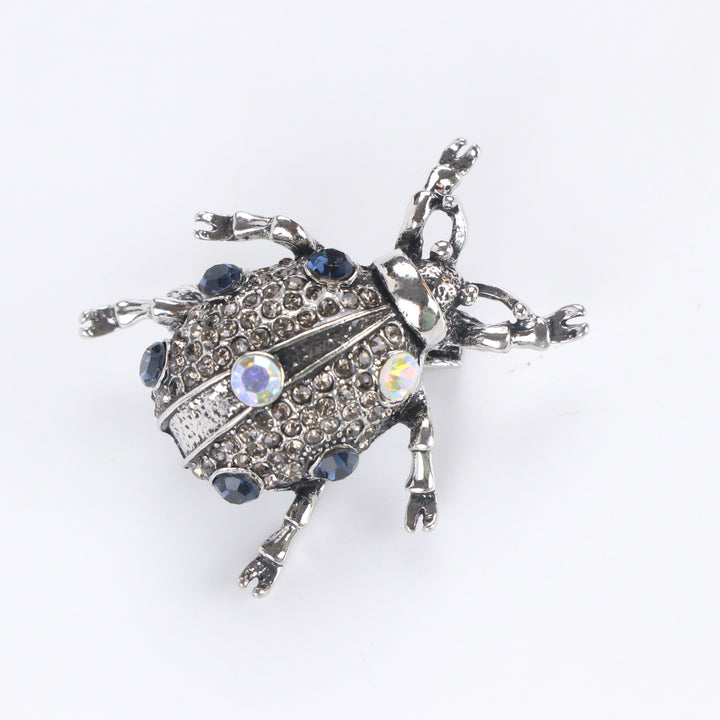 Antiqued silver-tone beetle brooch pin pavé-set with smoky rhinestones, blue crystals, and iridescent gems on a white background by Delemon