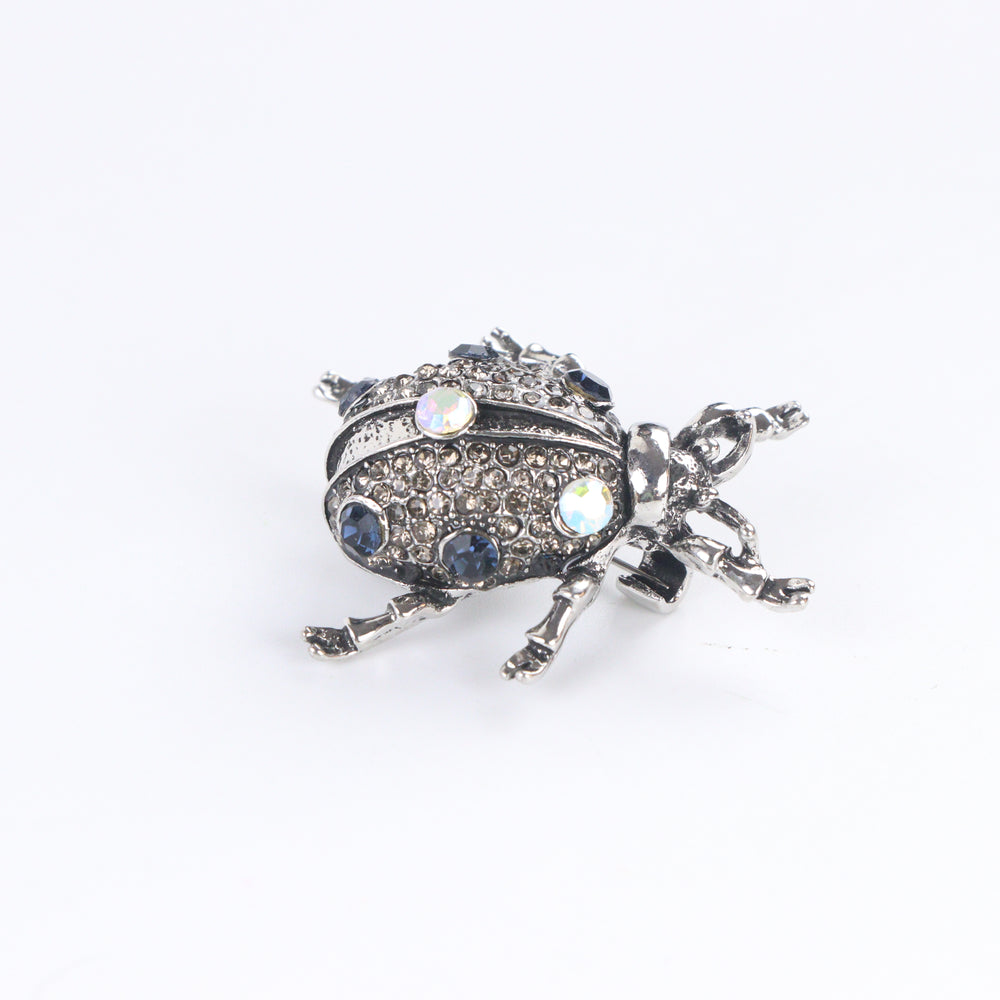 Antiqued silver-tone beetle brooch pin pavé-set with smoky rhinestones, blue crystals, and iridescent gems on a white background by Delemon
