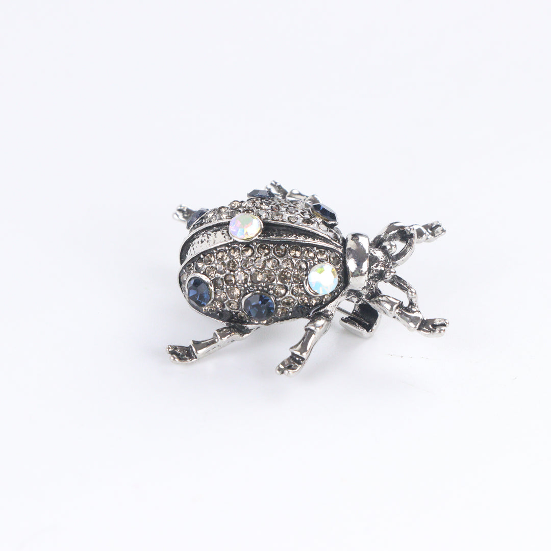 Antiqued silver-tone beetle brooch pin pavé-set with smoky rhinestones, blue crystals, and iridescent gems on a white background by Delemon