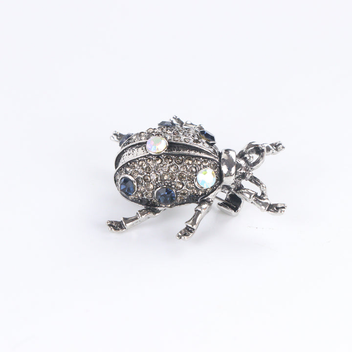 Antiqued silver-tone beetle brooch pin pavé-set with smoky rhinestones, blue crystals, and iridescent gems on a white background by Delemon