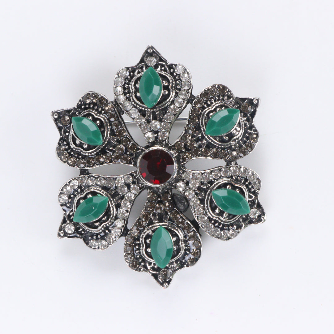 Antique silver-tone floral brooch pin with marquise green stones, paved rhinestones, and a ruby red center crystal on a white background by Delemon