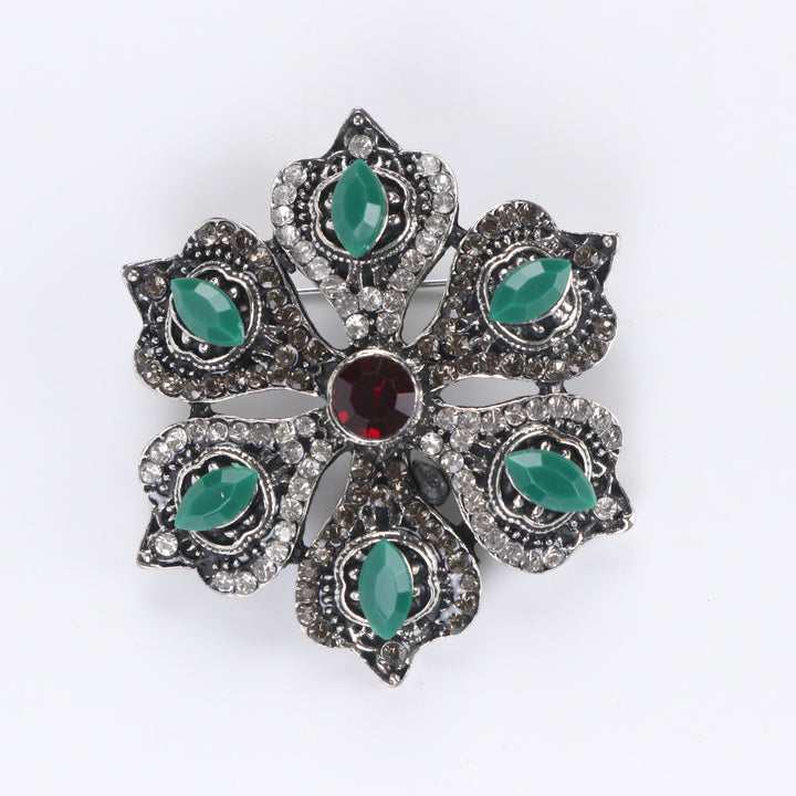 Antique silver-tone floral brooch pin with marquise green stones, paved rhinestones, and a ruby red center crystal on a white background by Delemon