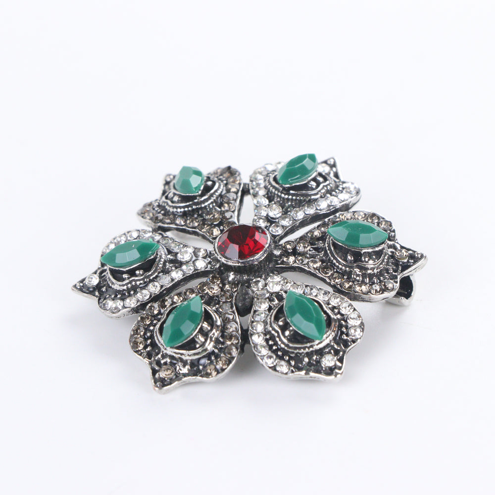 Antique silver-tone floral brooch pin with marquise green stones, paved rhinestones, and a ruby red center crystal on a white background by Delemon