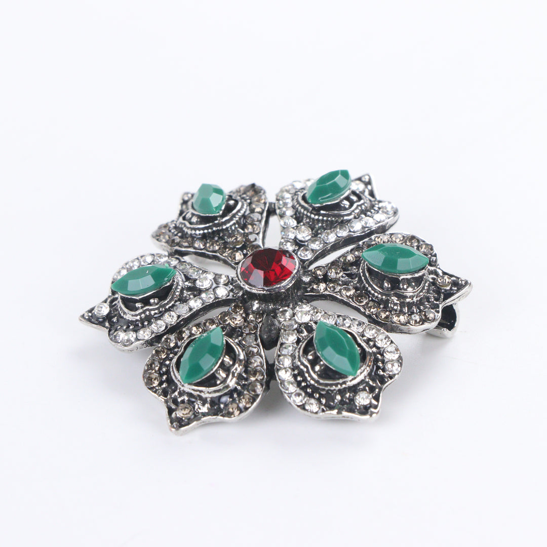 Antique silver-tone floral brooch pin with marquise green stones, paved rhinestones, and a ruby red center crystal on a white background by Delemon