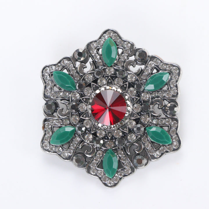 Antique silver-tone filigree starburst medallion brooch pin featuring a ruby red crystal center and jade green marquise accents on a white background by Delemon