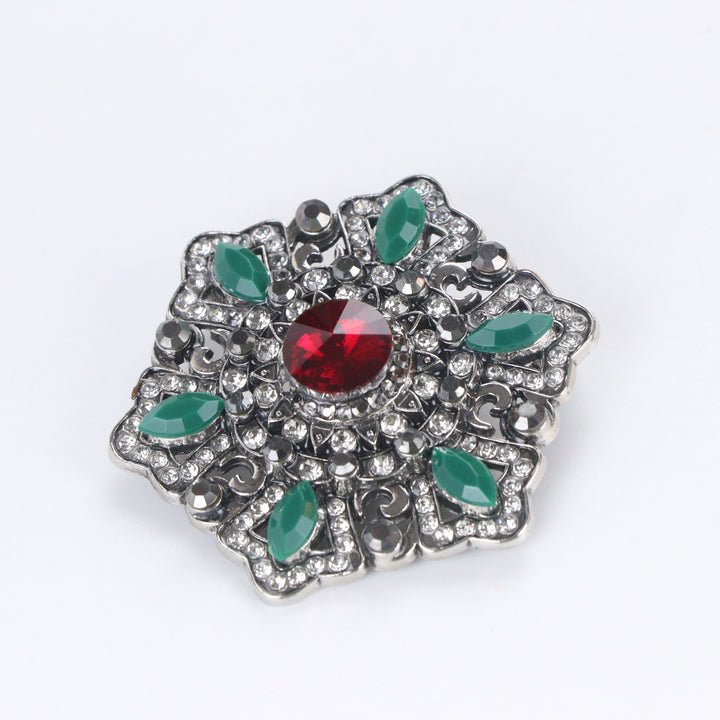 Antique silver-tone filigree starburst medallion brooch pin featuring a ruby red crystal center and jade green marquise accents on a white background by Delemon