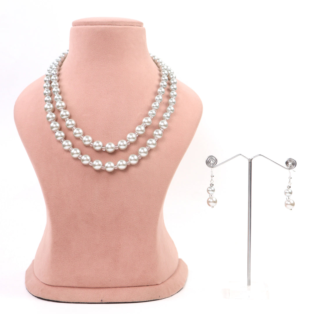 White double-strand glass pearl necklace with clear spacer beads and matching earrings on a pink display - De-Lemon Collection.